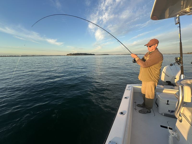 Angler fighting a fish at sunset with the Boston skyline behind