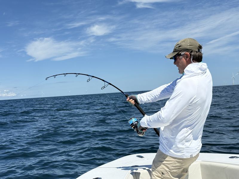 Angler fighting a fish with a deep bent rod under blue skies