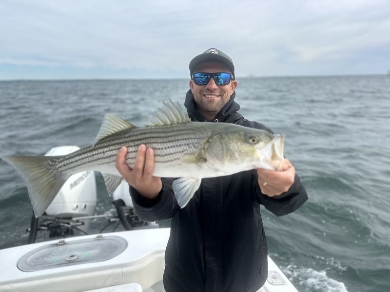 Angler holding a big striped bass with spray behind