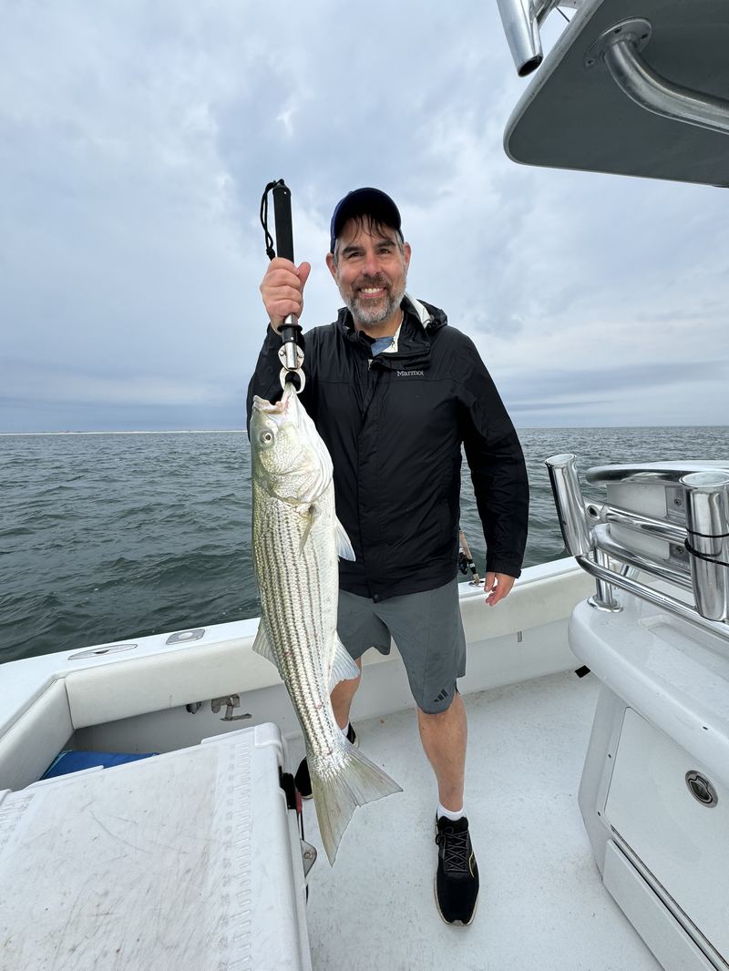 Angler holding up a big striped bass aboard the Conch 27